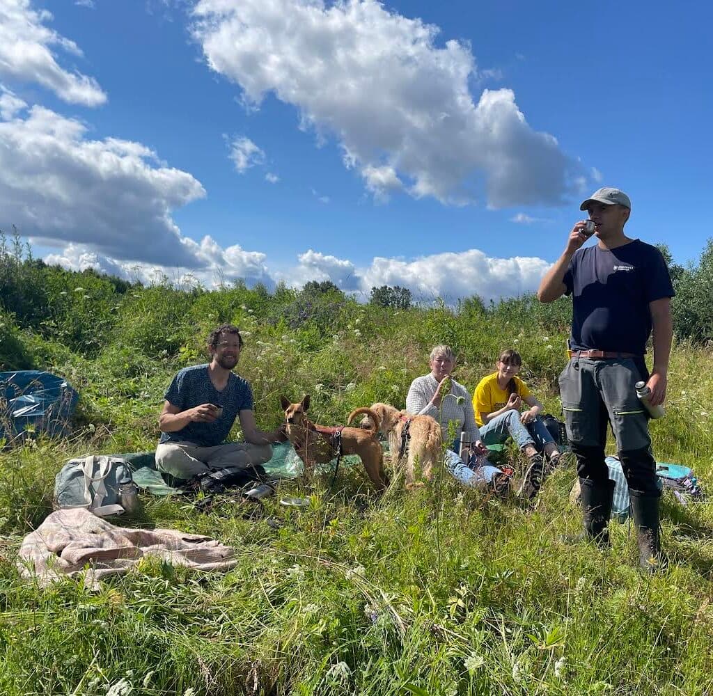 en grupp människor i gröngräset med arbetsredskap runt sig. En står upp och dricker kaffe.