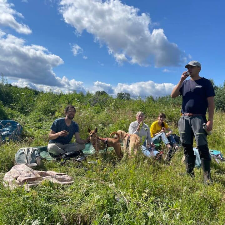 en grupp människor i gröngräset med arbetsredskap runt sig. En står upp och dricker kaffe.