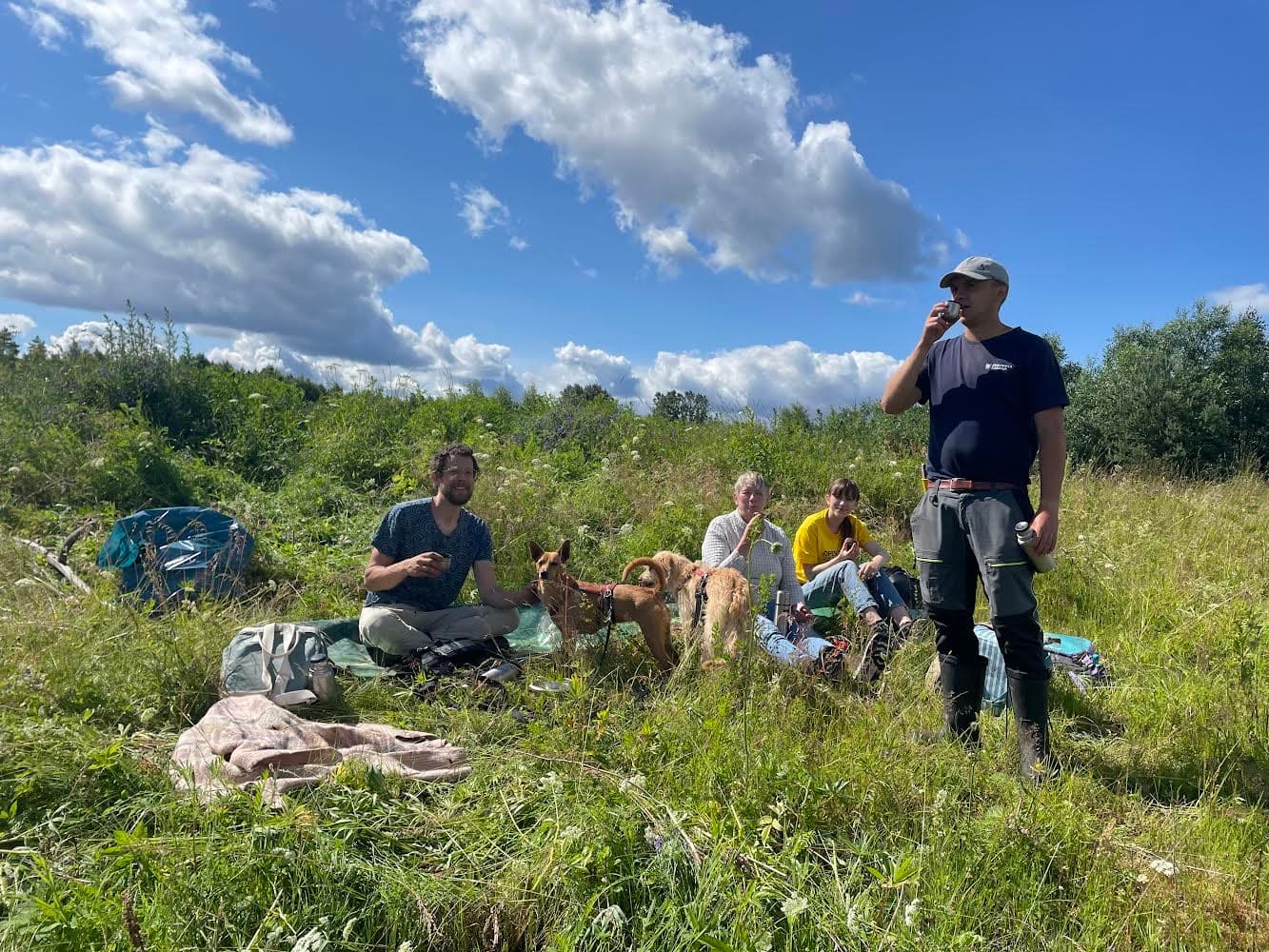en grupp människor i gröngräset med arbetsredskap runt sig. En står upp och dricker kaffe.