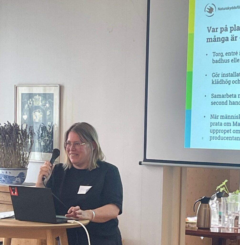 en kvinna står vid datorn och presenterar. Bakom skymtar presentationen med Naturskyddsföreningens logotyp.
